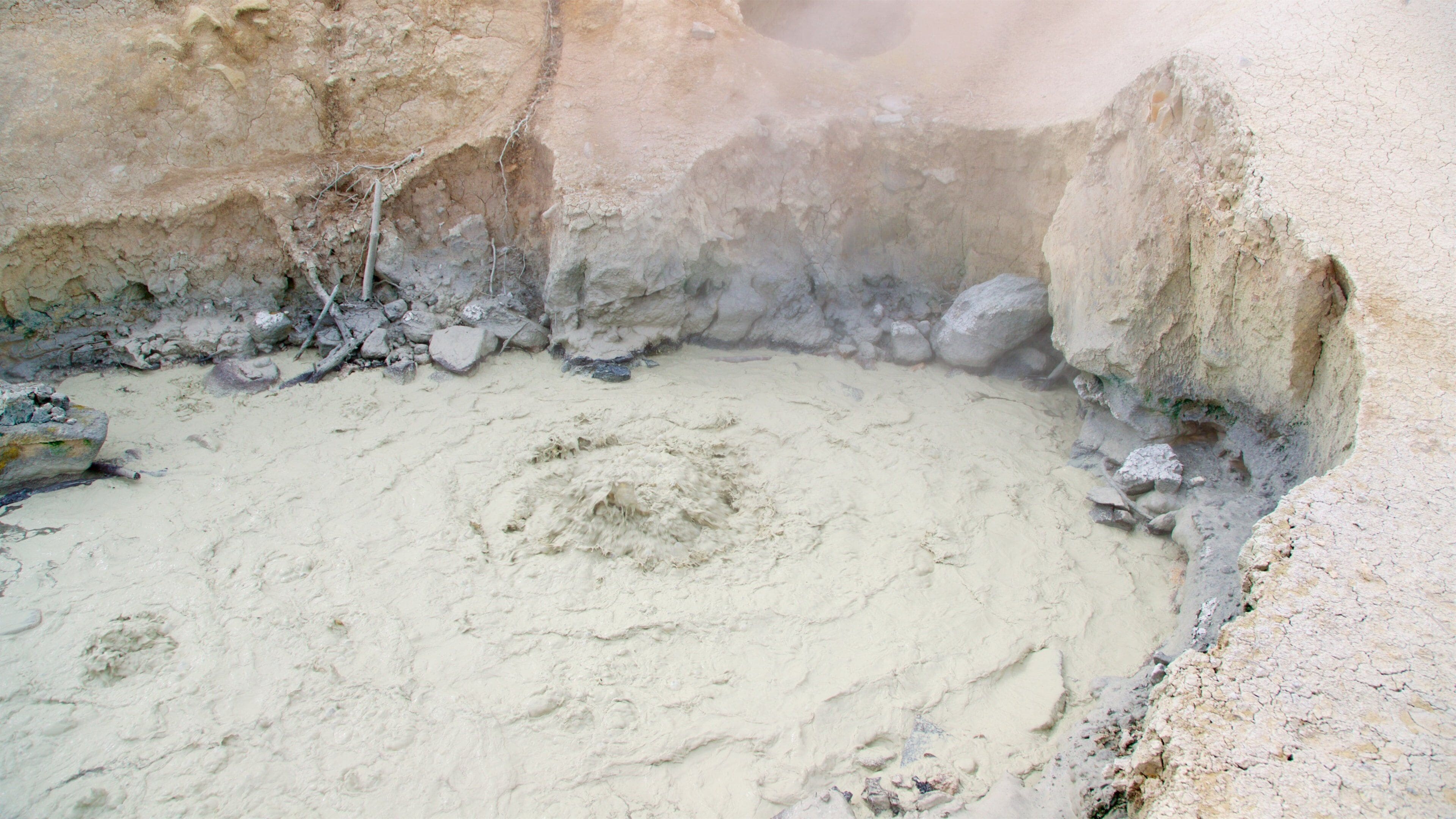 A geothermal area with a circular hot spring surrounded by rocky terrain.