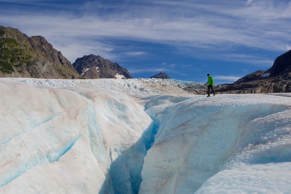 A glacier with a person in a green jacket standing on it.
