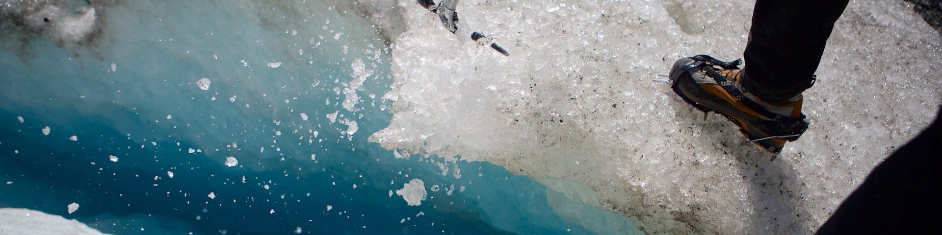 Una persona usando una herramienta para romper hielo cerca de un cuerpo de agua azul.