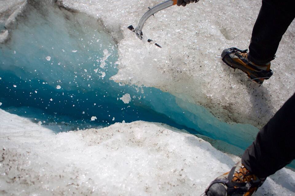 Una persona usando una herramienta para romper hielo cerca de un cuerpo de agua azul.