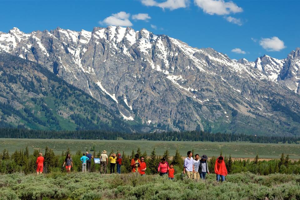 A group of people hiking in a mountainous area with snow-capped peaks in the background.