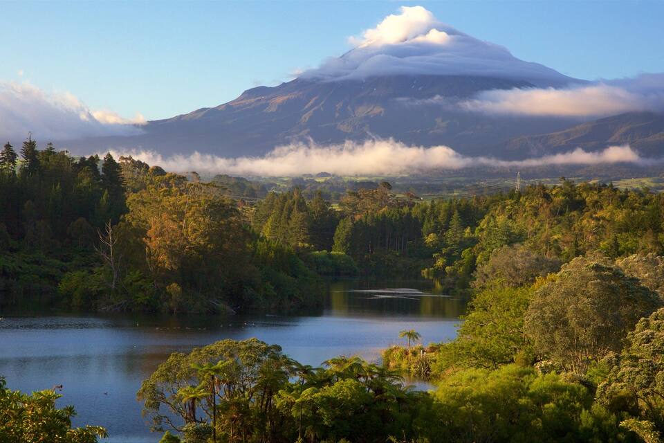 A lake surrounded by dense forest and a mountain with clouds.
