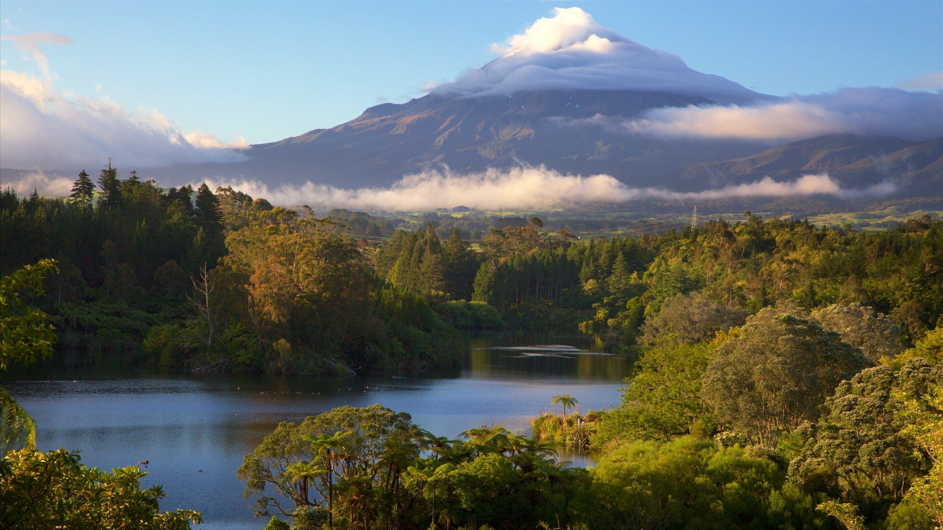A lake surrounded by dense forest and a mountain with clouds.