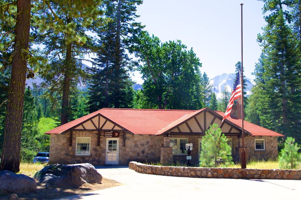 A stone ranger station with a red roof, surrounded by tall trees and a mountain in the background.