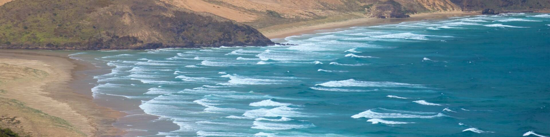 A coastal landscape with a sandy beach, rocky cliffs, and a clear blue ocean.