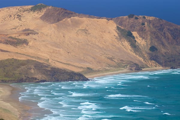 Un paysage côtier avec une plage de sable, des falaises rocheuses et un océan bleu limpide.