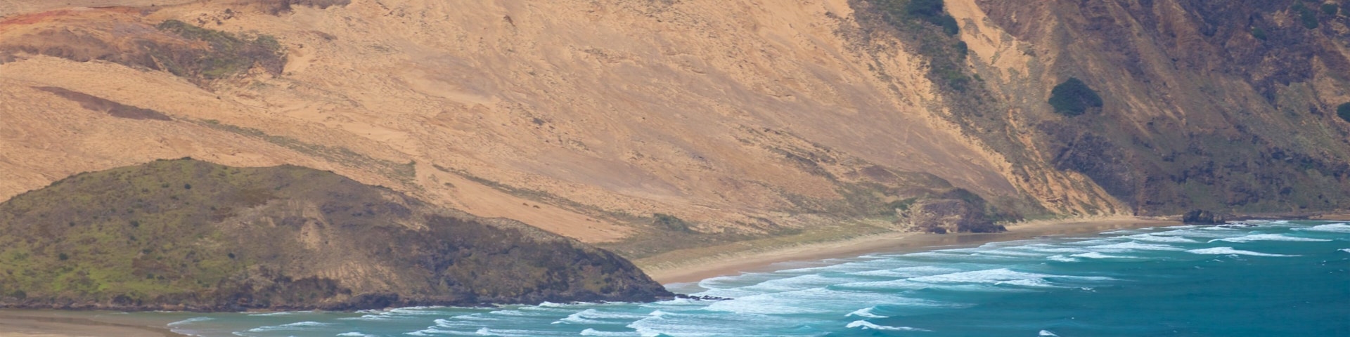 Paisagem costeira com uma praia arenosa, falésias rochosas e oceano azul cristalino.