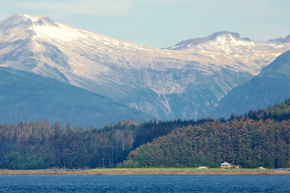 Cordillera montañosa con picos nevados, bosque denso y un cuerpo de agua con barcos.