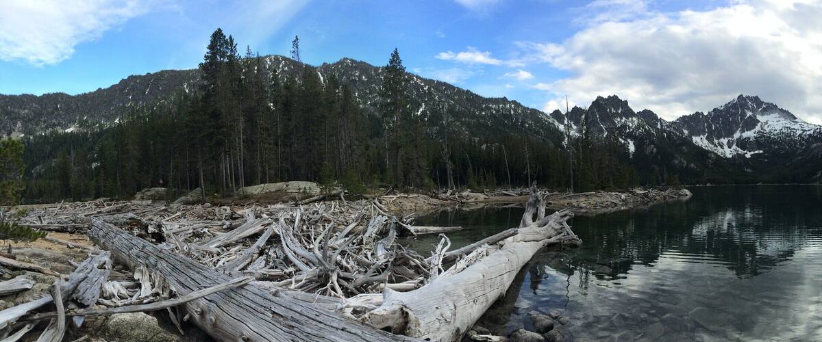 A calm lake surrounded by mountains with snow-capped peaks and dense forests.