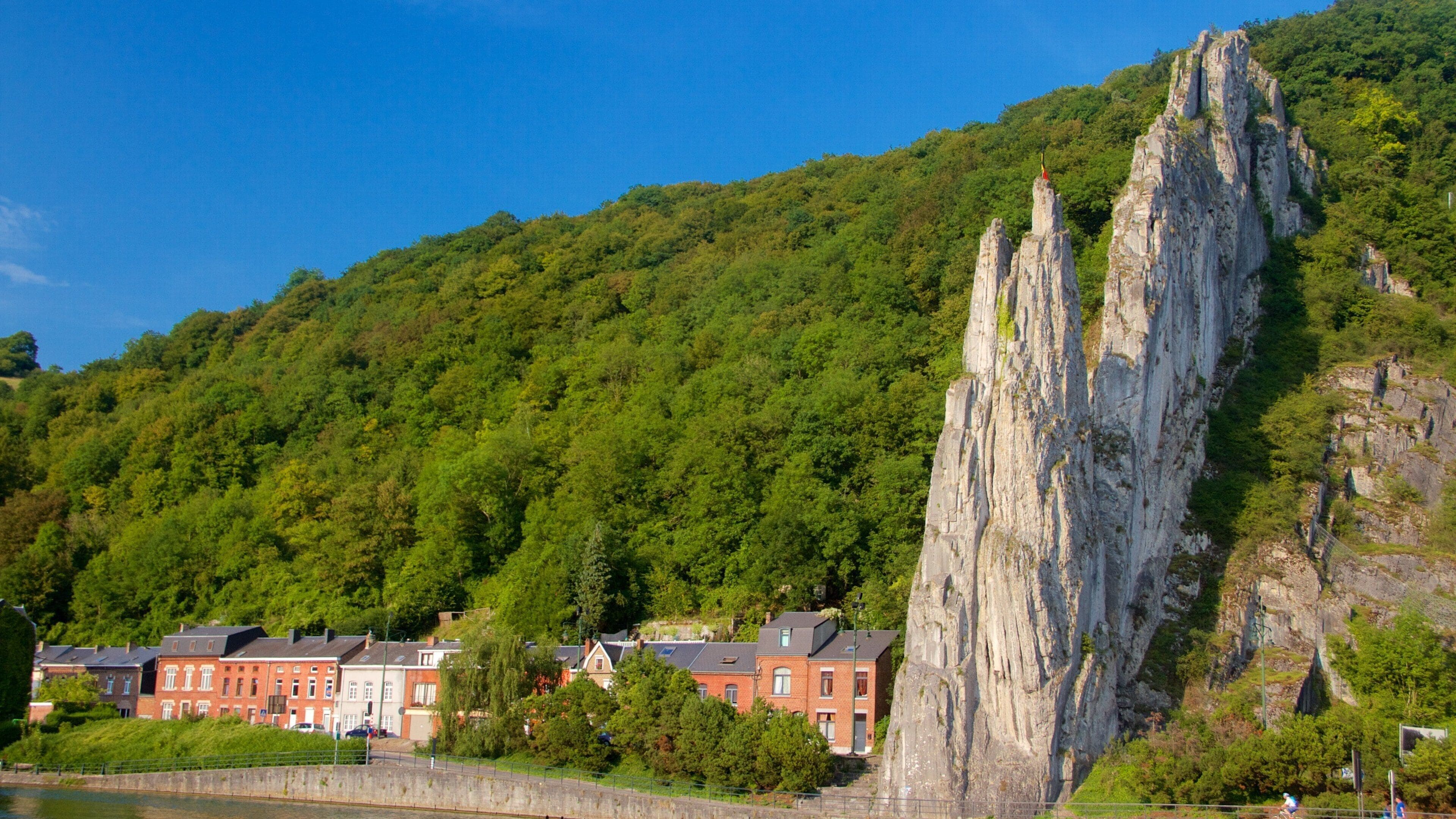 A rocky cliff, a river, and red buildings on a hillside.