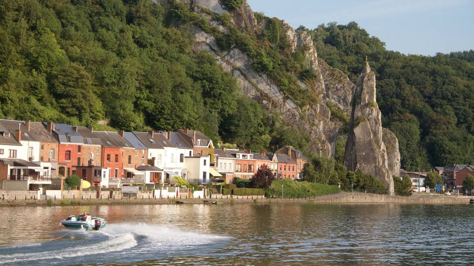 A lake with houses along the shore, a boat speeding across the water, and a large rock formation in the background.