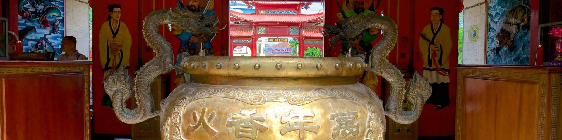 A large ornate bronze vessel with dragons, set in a temple with red walls and traditional Chinese paintings.