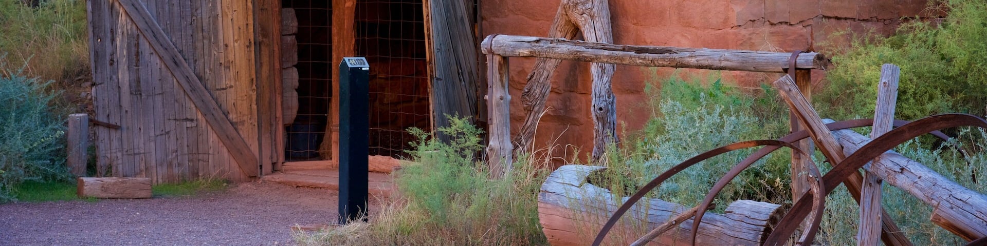 A rustic wooden cabin with a red roof, surrounded by dry grass and shrubs.