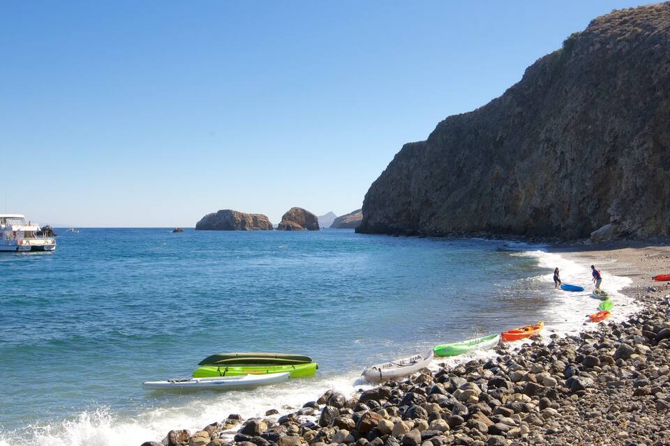 Una platja rocosa amb kayaks i un vaixell a l'aigua.