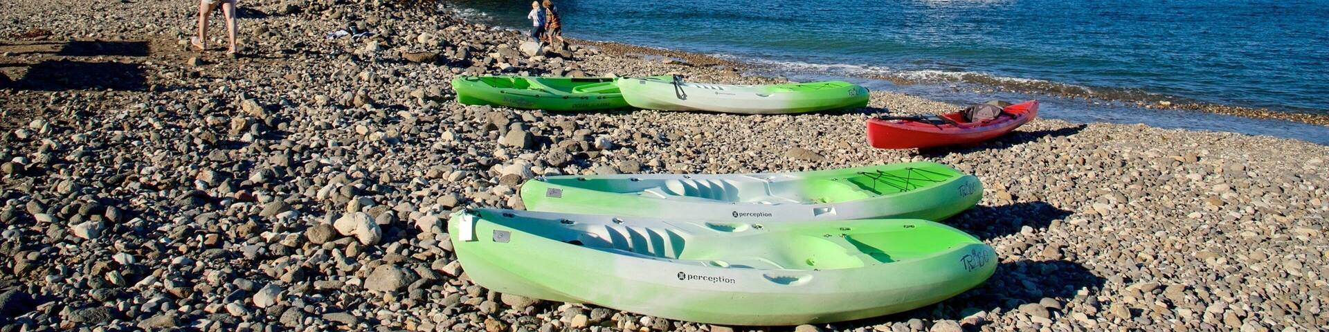 A rocky beach with kayaks, a white boat, and a rocky cliff.