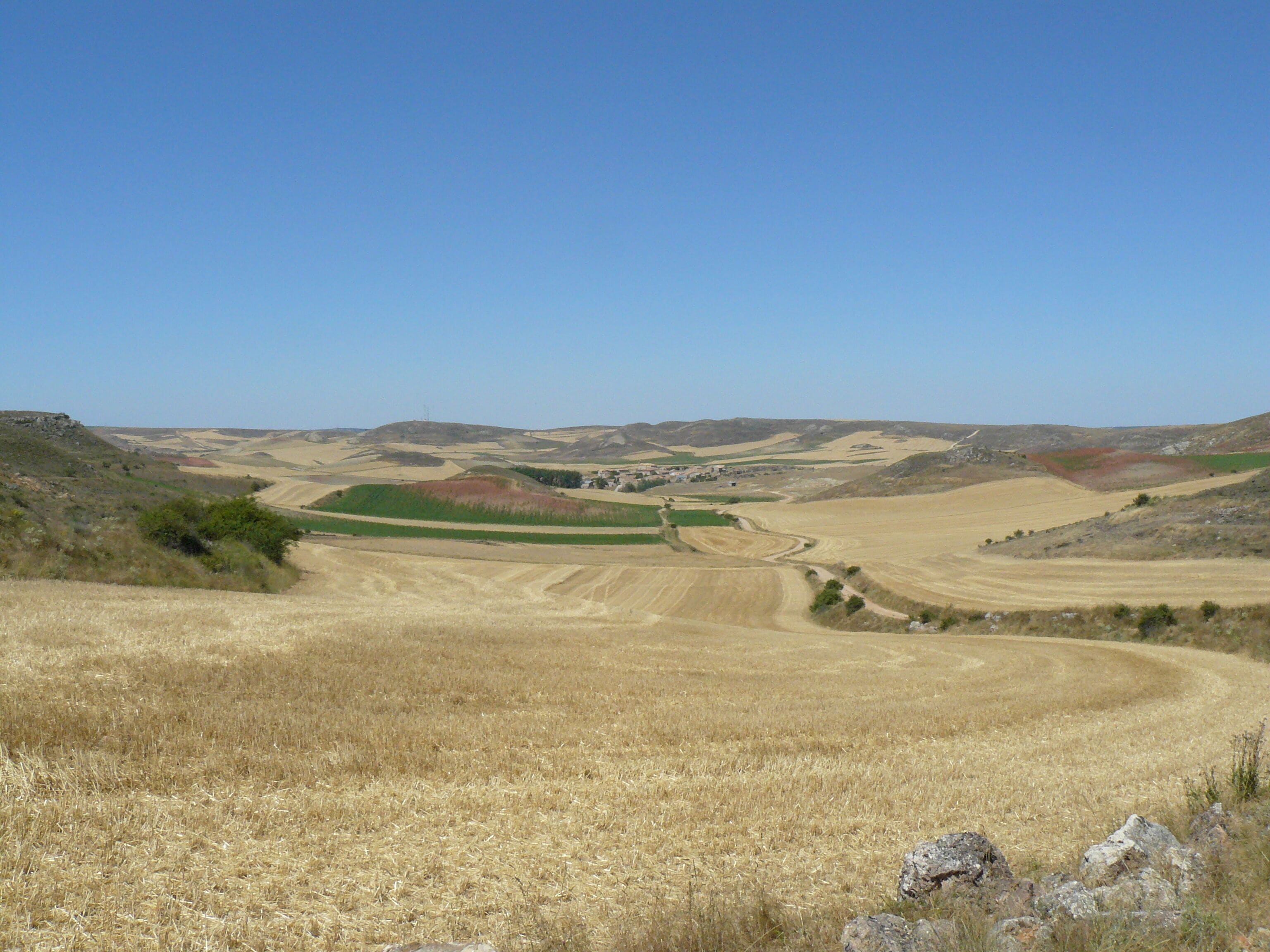A vast agricultural landscape with rolling hills, fields, and a clear blue sky.