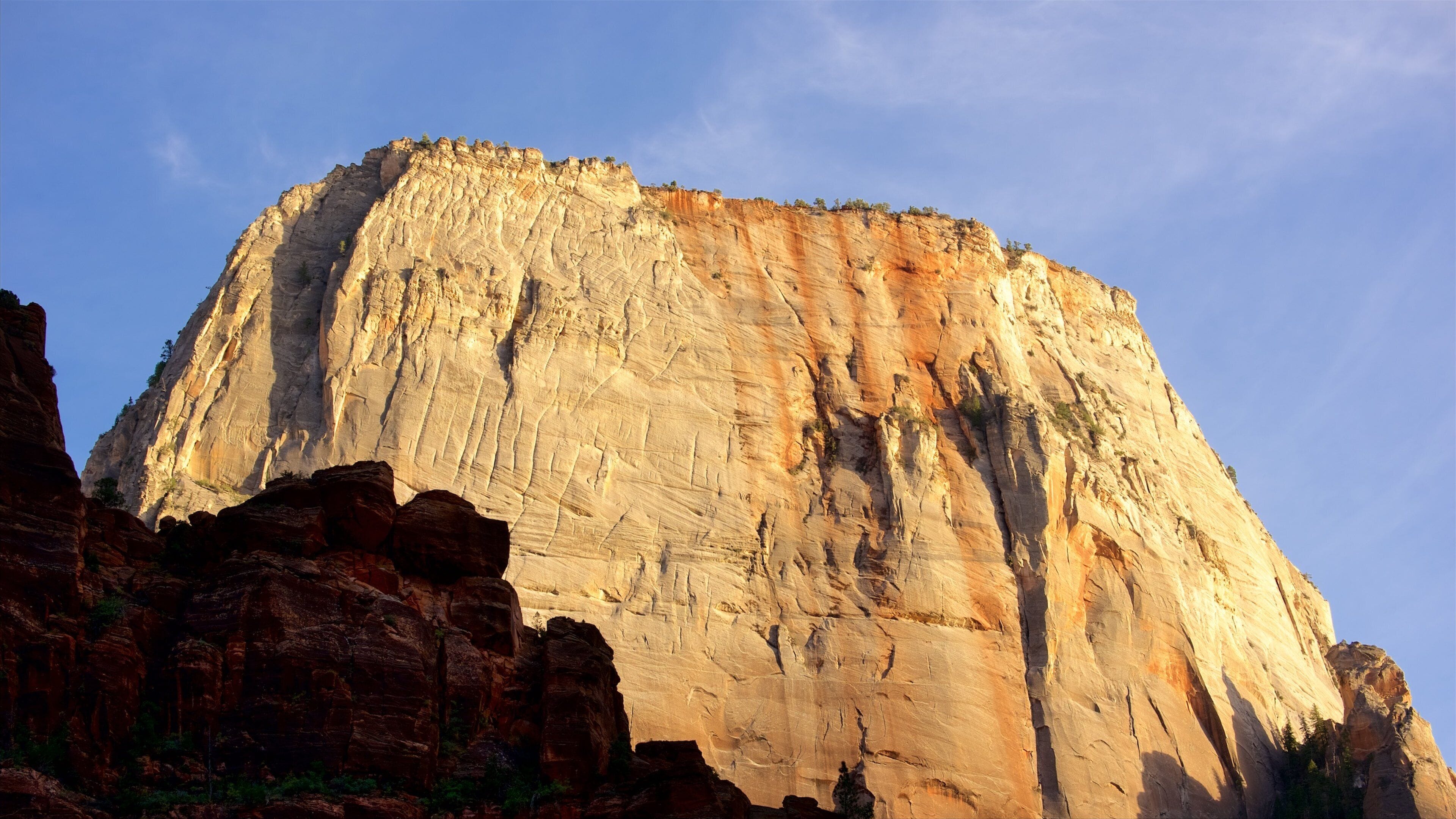A large, rugged mountain with a flat top, surrounded by red rock formations and sparse vegetation.