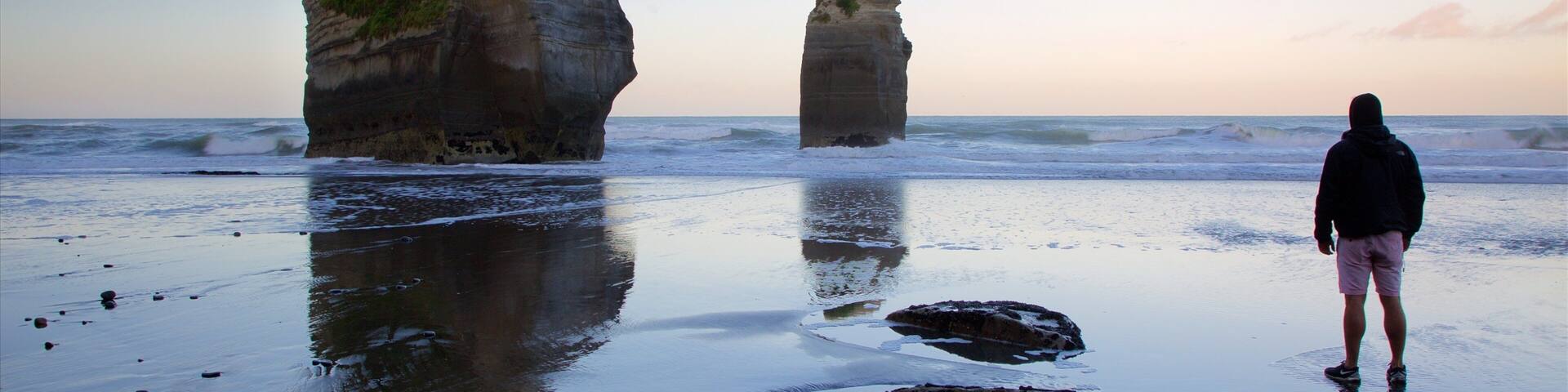A person standing on a beach with large rock formations in the background.