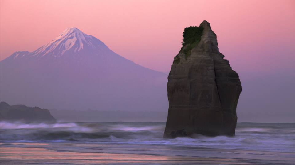 A coastal rock formation with a mountain in the background.