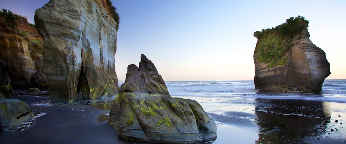 A coastal landscape with large rock formations and a beach.