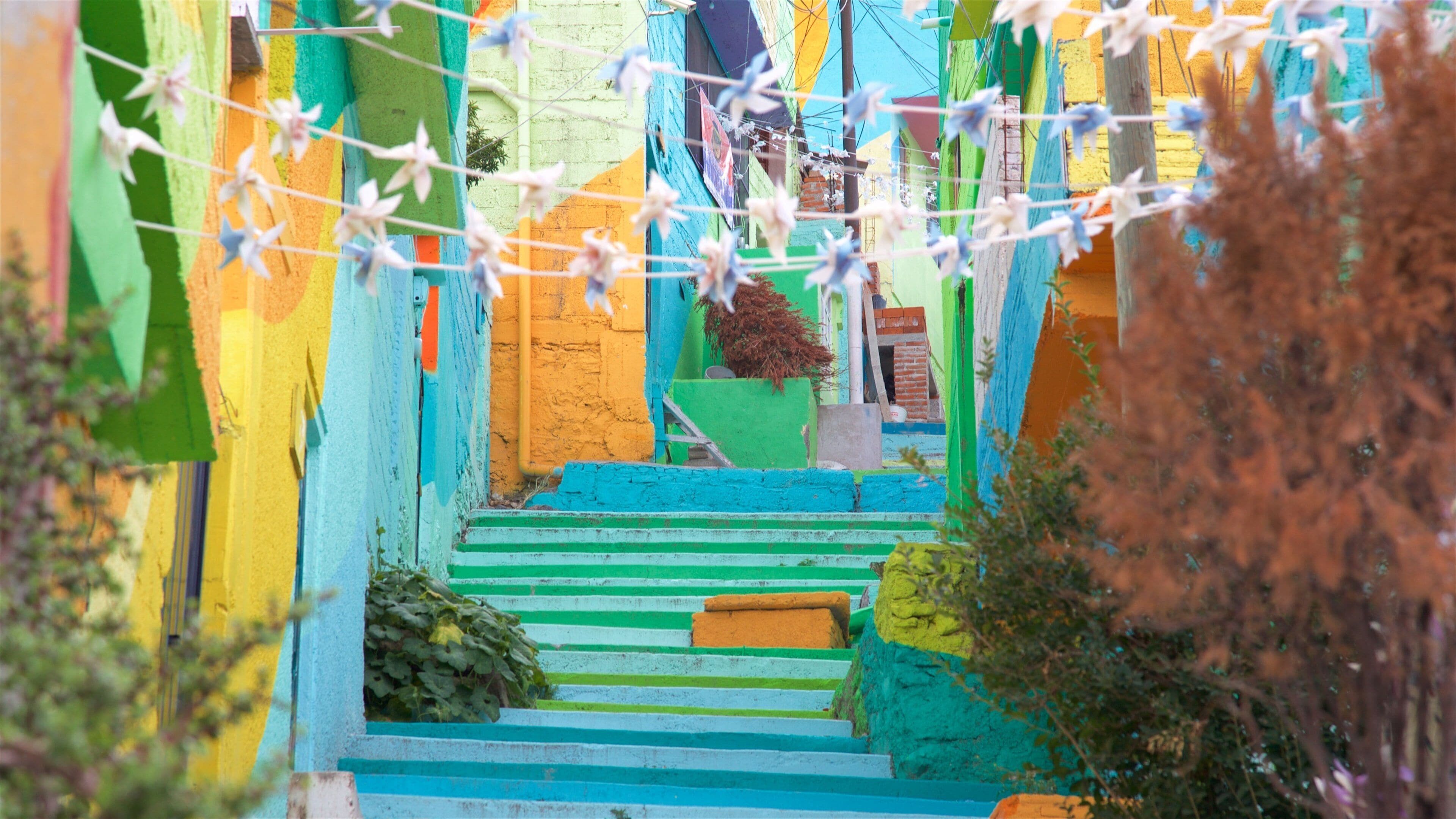 Una escalera colorida con escalones verdes, amarillos y azules que suben a un edificio con una puerta azul.