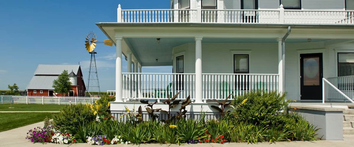 A white two-story house with a balcony, surrounded by a garden with various flowers.