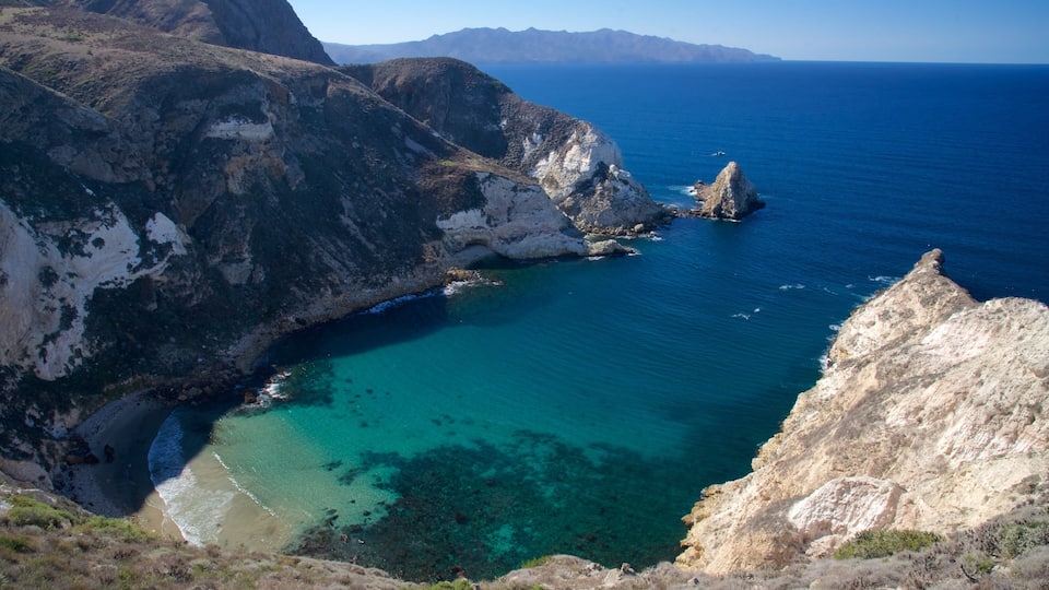 A coastal landscape with cliffs, clear turquoise waters, and distant mountains.