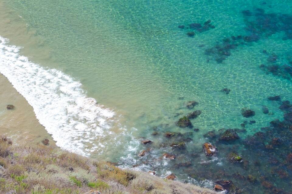 Paisatge costaner amb aigües turqueses cristal·lines, platja sorrenca i roques.