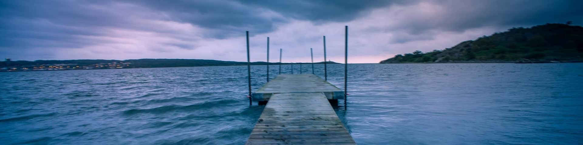 A wooden pier extending into a body of water under a cloudy sky.