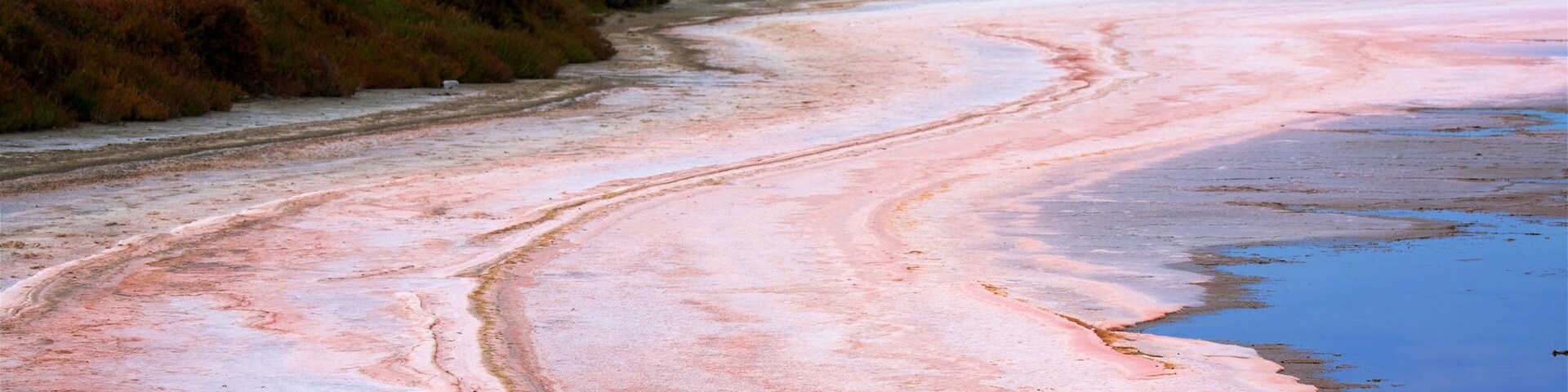 Una extensión de sal rosa con un camino serpenteante y un cuerpo de agua.