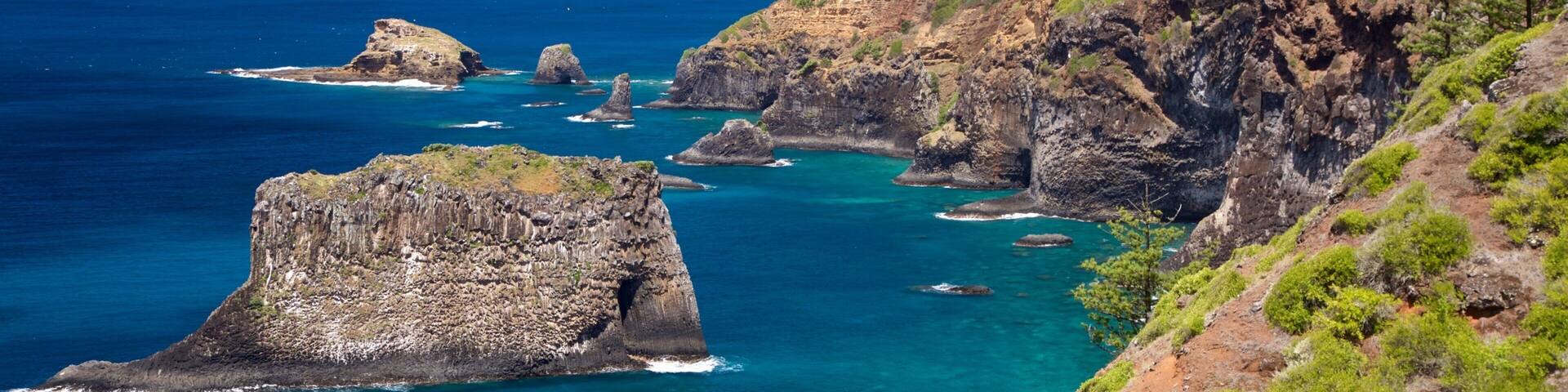 A coastal landscape with rocky cliffs, clear blue waters, and green vegetation.