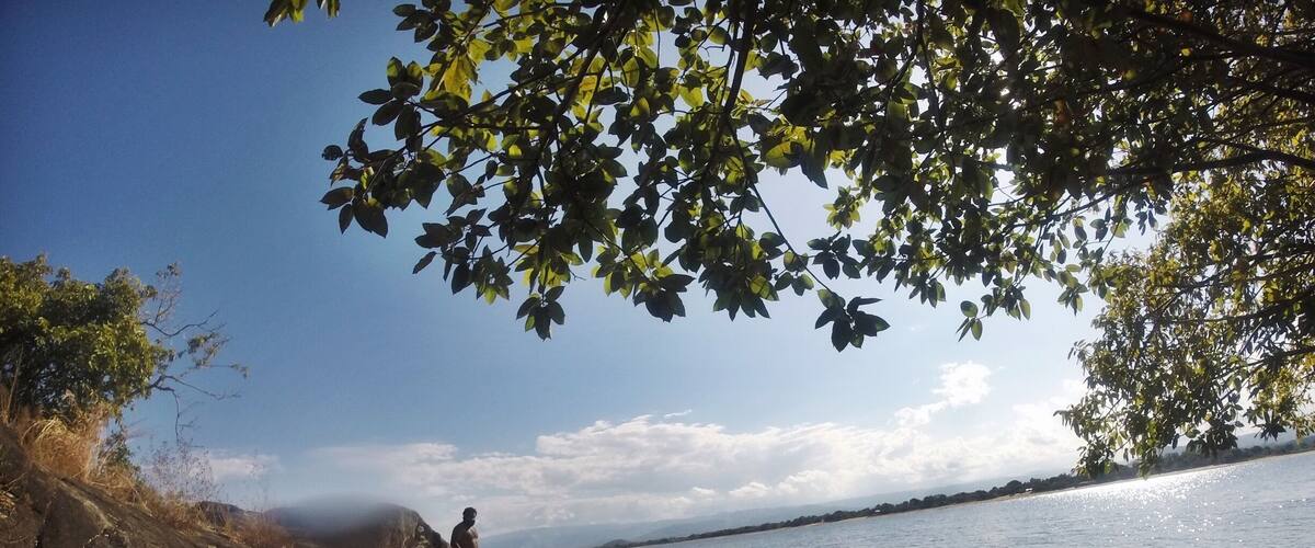 A rocky shoreline with people enjoying the water, a clear sky, and distant mountains.