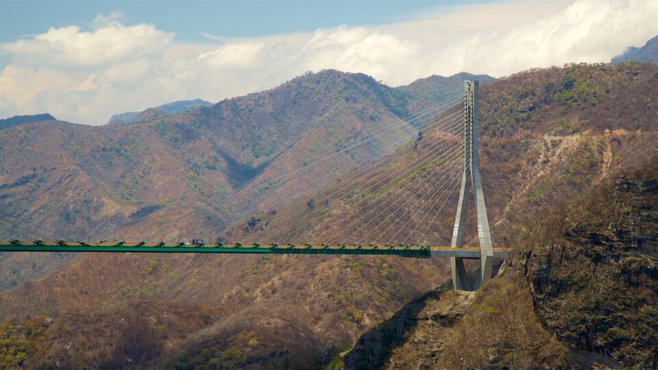 A cable-stayed bridge spanning a deep gorge with steep, forested mountains in the background.