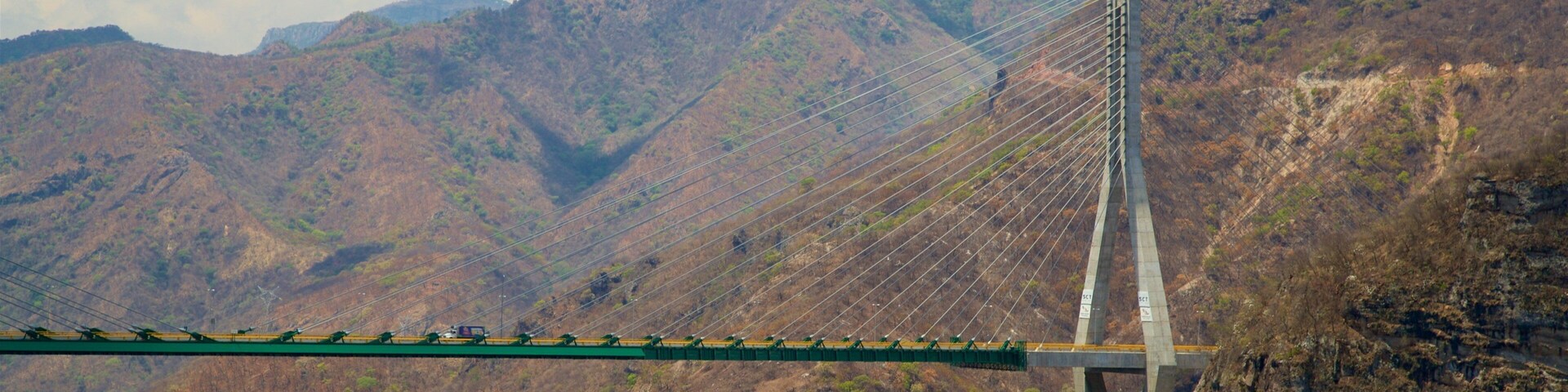 Un puente atirantado cruza un desfiladero profundo con montañas boscosas y empinadas al fondo.