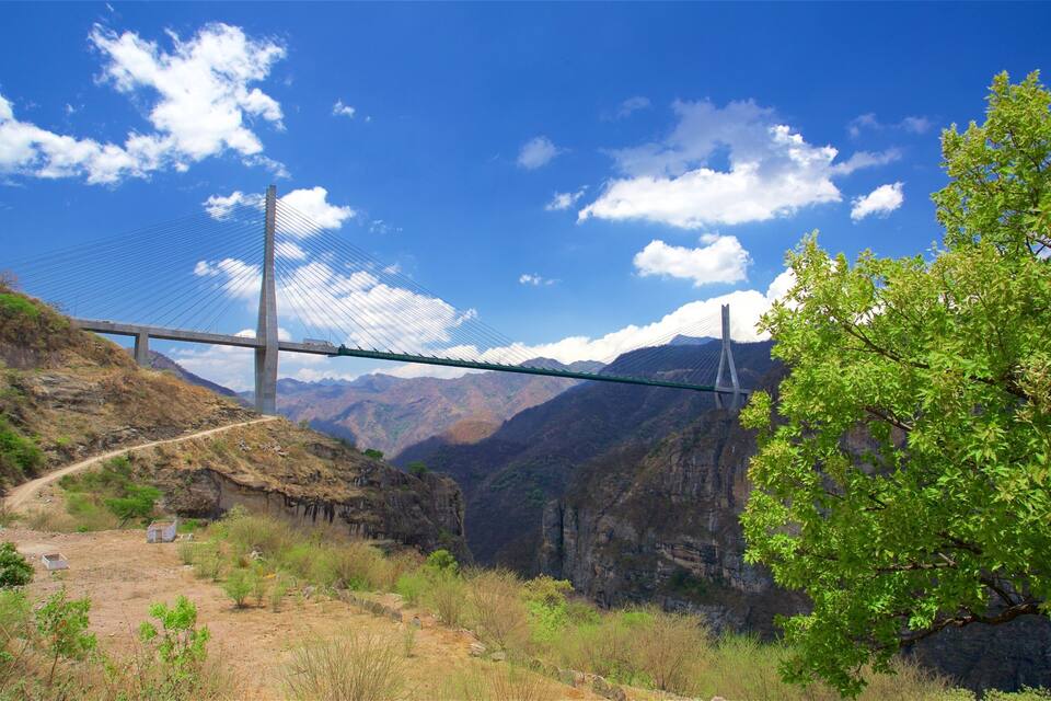 A suspension bridge over a valley with mountains in the background.