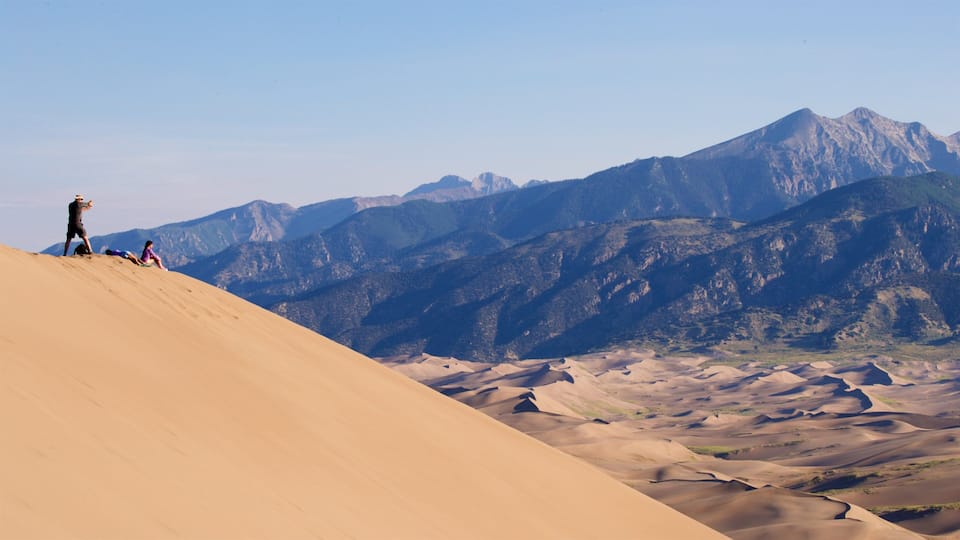 A desert landscape with sand dunes and mountains in the background.