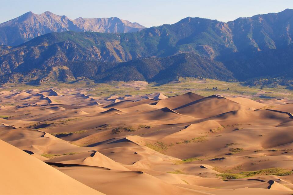 A desert landscape with sand dunes and mountains in the background.