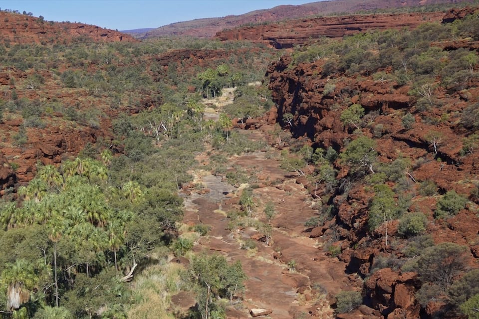A rugged landscape with red rock formations, green vegetation, and a narrow canyon.