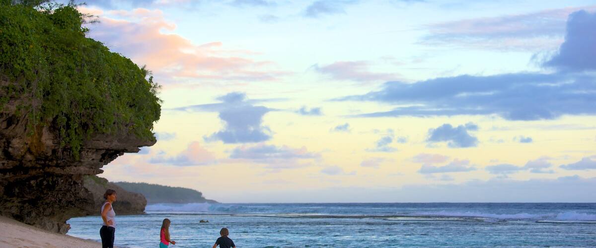 A beach with a rocky cliff, ocean waves, and a sunset sky.
