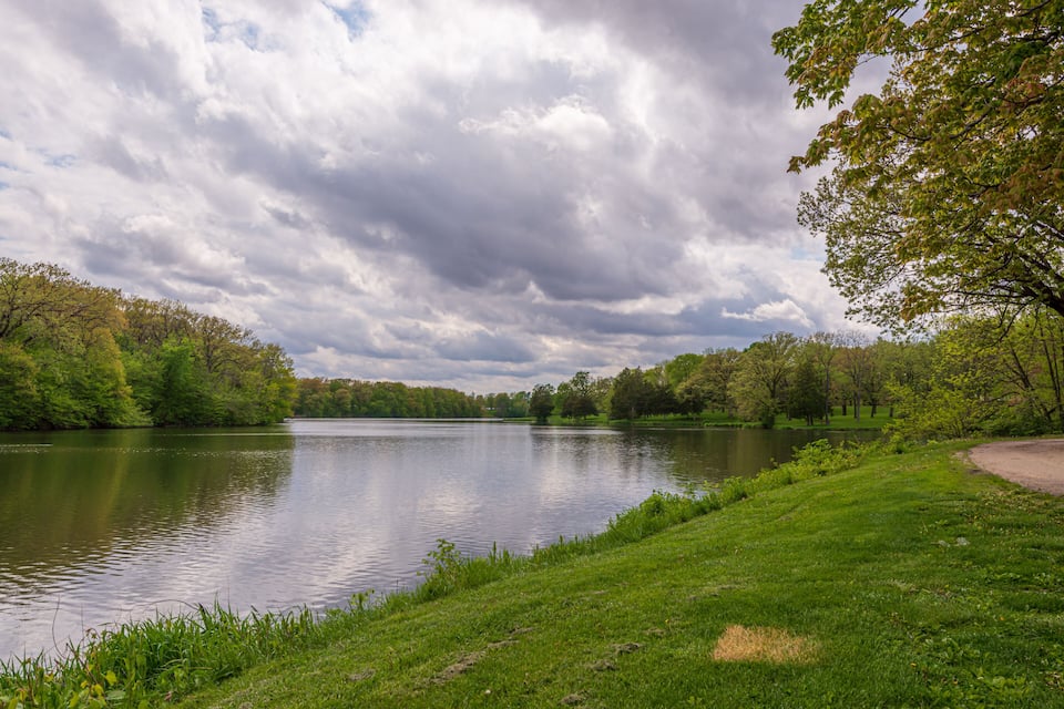 A calm lake surrounded by lush green trees and a cloudy sky.