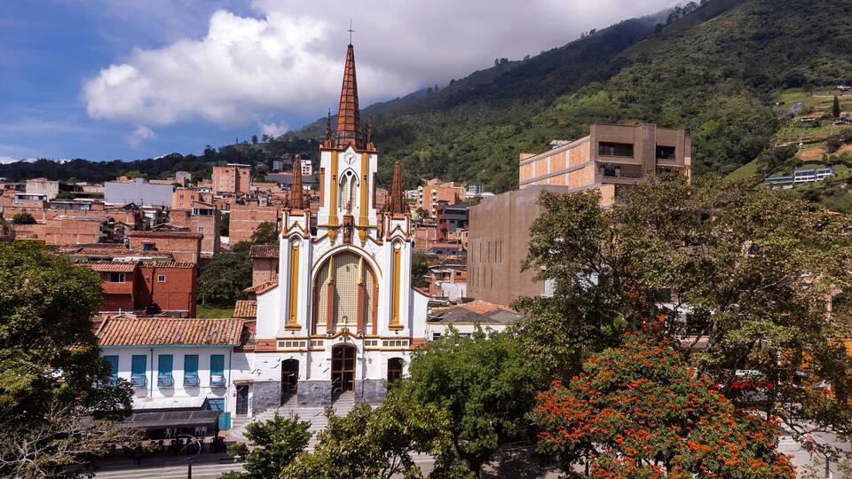A church with a tall spire, surrounded by residential buildings and a hillside.