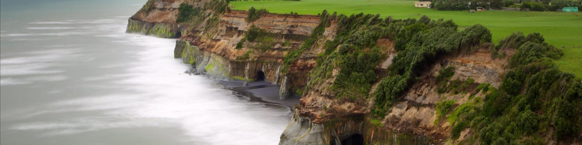 A coastal landscape with cliffs, a body of water, and distant hills.