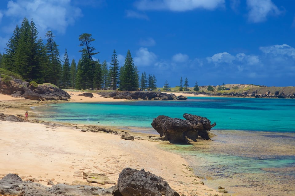 Una platja amb aigua turquesa cristal·lina, sorra daurada i roques.