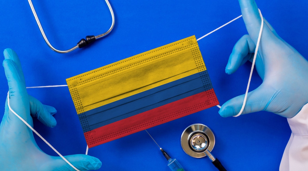 Medical mask with the flag of Colombia in the hands of a doctor and stethoscope, flat lay. Coronavirus pandemic