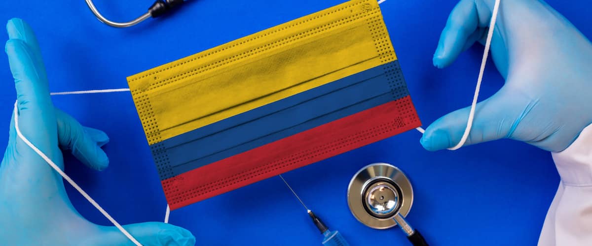 Medical mask with the flag of Colombia in the hands of a doctor and stethoscope, flat lay. Coronavirus pandemic