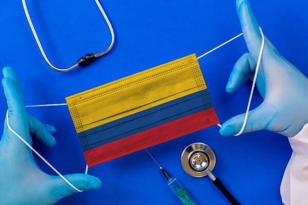 Medical mask with the flag of Colombia in the hands of a doctor and stethoscope, flat lay. Coronavirus pandemic