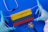Medical mask with the flag of Colombia in the hands of a doctor and stethoscope, flat lay. Coronavirus pandemic