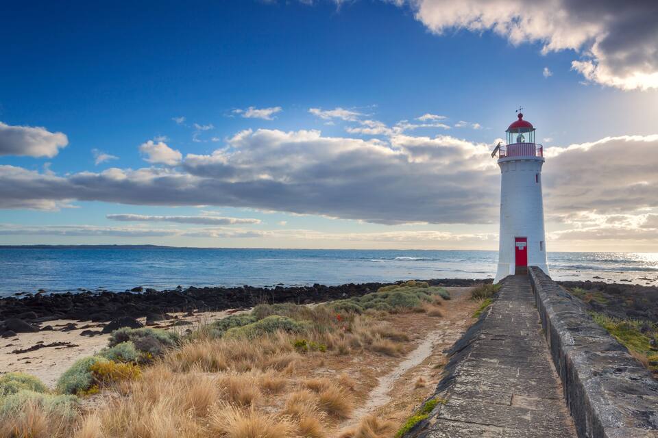 A lighthouse on a rocky coastline with a clear sky and ocean in the background.