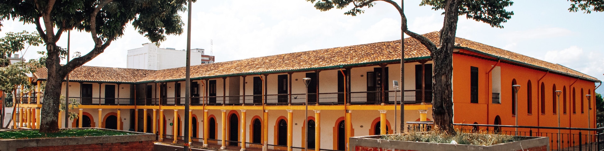 Un patio con suelo de baldosas, un edificio de paredes amarillas y anaranjadas, y árboles.