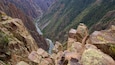 Eine Schlucht mit einem Fluss, der sich hindurchschlängelt, umgeben von felsigen Klippen und spärlicher Vegetation.